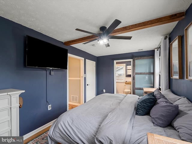 bedroom with beamed ceiling, ceiling fan, a textured ceiling, and ensuite bath