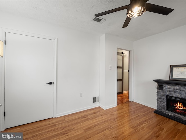 unfurnished living room featuring ceiling fan, a textured ceiling, a fireplace, and light hardwood / wood-style flooring