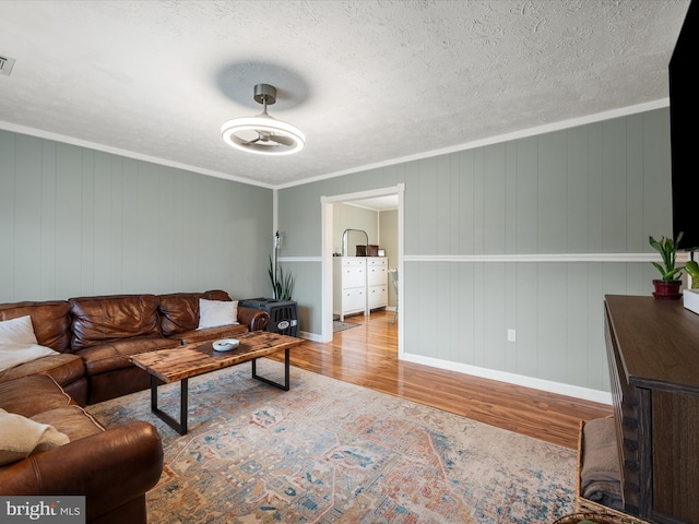 living room with crown molding, ceiling fan, a textured ceiling, and light wood-type flooring