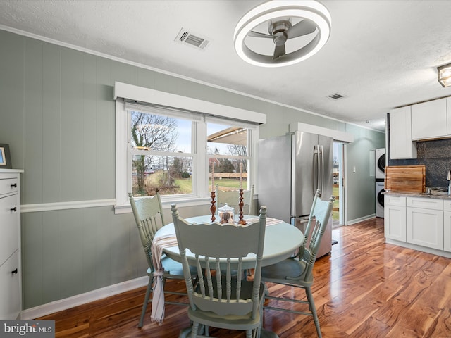 dining space featuring crown molding, stacked washer and clothes dryer, and wood-type flooring