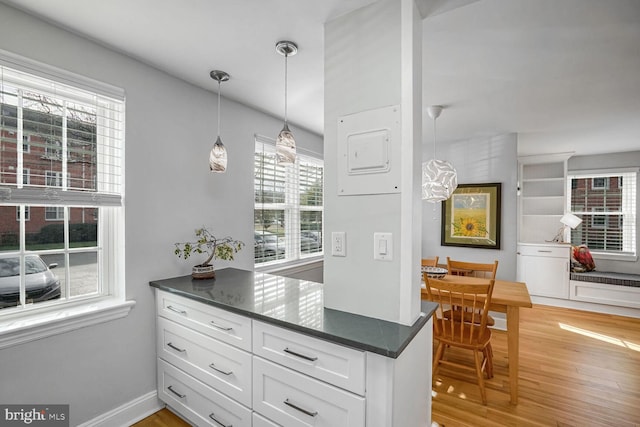 kitchen with white cabinetry, decorative light fixtures, kitchen peninsula, and light hardwood / wood-style floors