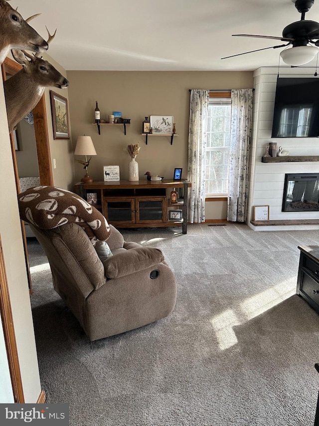 living room with ceiling fan, a large fireplace, and carpet flooring