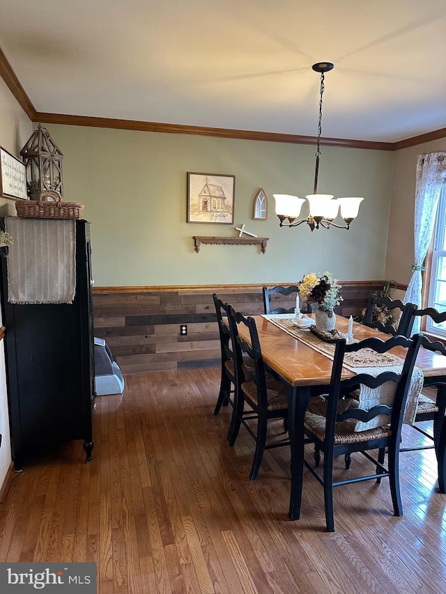 dining space with crown molding, hardwood / wood-style floors, a notable chandelier, and wood walls