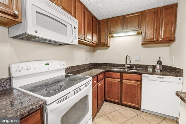 kitchen with sink, dark stone countertops, light tile patterned floors, white appliances, and a textured ceiling