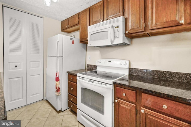 kitchen featuring light tile patterned flooring, dark stone countertops, a textured ceiling, and white appliances