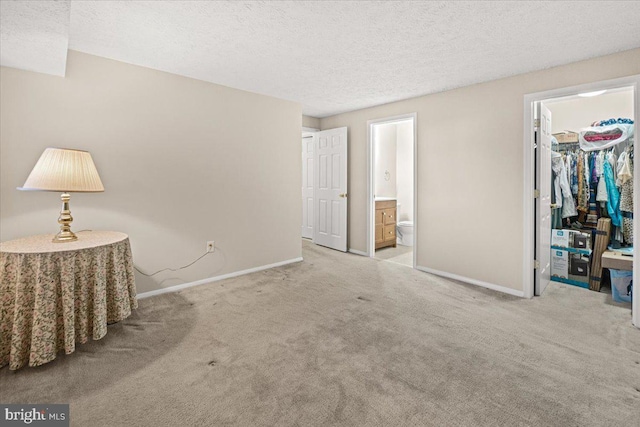 unfurnished bedroom featuring a walk in closet, light colored carpet, a textured ceiling, and ensuite bath