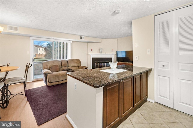 kitchen featuring kitchen peninsula, light tile patterned floors, a textured ceiling, and dark stone countertops