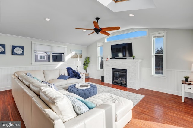 living room featuring ceiling fan, a stone fireplace, hardwood / wood-style floors, and lofted ceiling with skylight