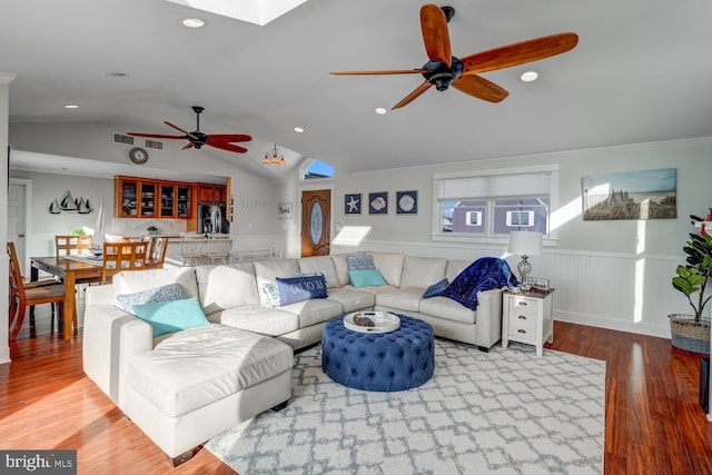 living room featuring hardwood / wood-style flooring, lofted ceiling with skylight, ornamental molding, and ceiling fan