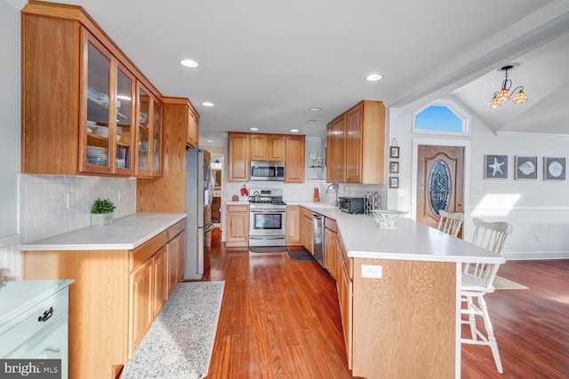 kitchen featuring vaulted ceiling, pendant lighting, a kitchen bar, stainless steel appliances, and light wood-type flooring