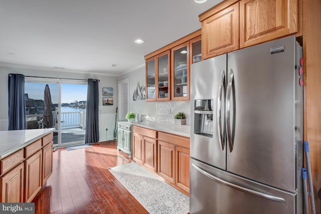 kitchen featuring dark hardwood / wood-style flooring, decorative backsplash, stainless steel fridge with ice dispenser, crown molding, and a water view