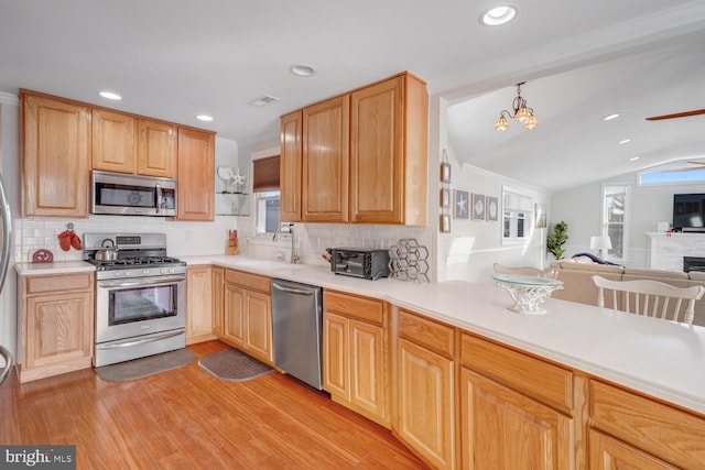 kitchen with sink, appliances with stainless steel finishes, hanging light fixtures, light brown cabinetry, and light wood-type flooring