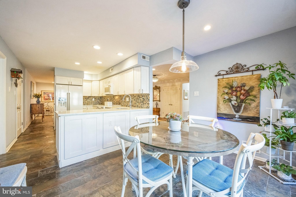 kitchen with white cabinetry, backsplash, hanging light fixtures, built in refrigerator, and kitchen peninsula