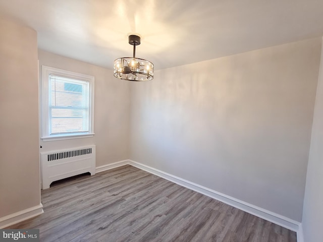 spare room with an inviting chandelier, radiator heating unit, and light wood-type flooring