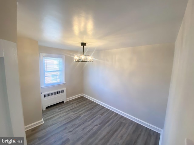 spare room with dark wood-type flooring, radiator, and a notable chandelier