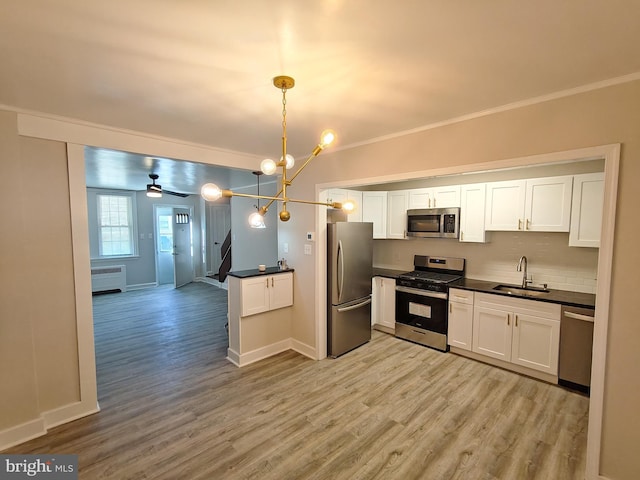 kitchen featuring sink, radiator, appliances with stainless steel finishes, white cabinetry, and decorative light fixtures