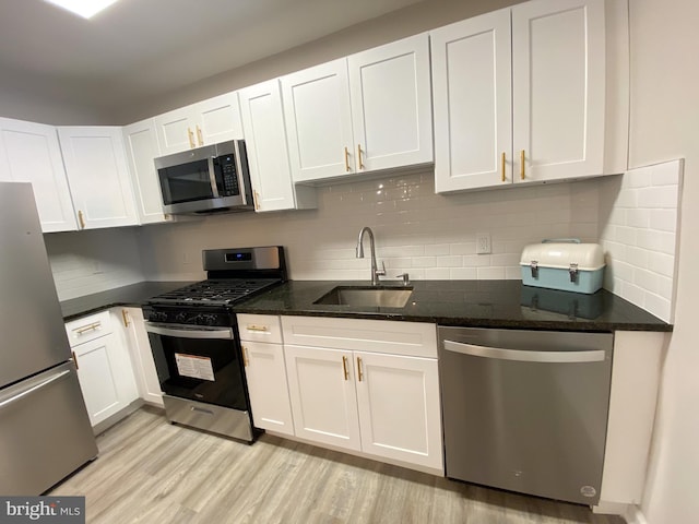 kitchen featuring sink, appliances with stainless steel finishes, white cabinetry, dark stone counters, and light wood-type flooring