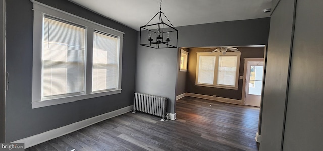 unfurnished dining area with radiator heating unit, dark hardwood / wood-style floors, and ceiling fan with notable chandelier