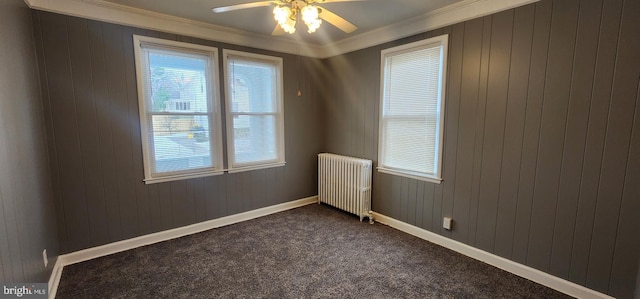 spare room featuring radiator heating unit, ornamental molding, ceiling fan, and dark colored carpet