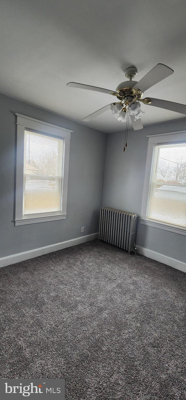 carpeted empty room with ceiling fan and radiator heating unit