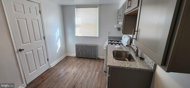 kitchen with radiator, sink, dark hardwood / wood-style flooring, light stone counters, and white gas stove