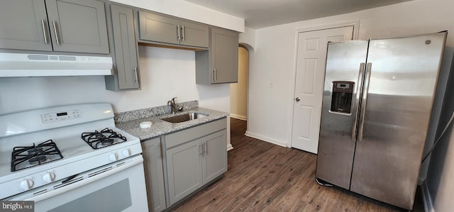 kitchen with sink, dark hardwood / wood-style floors, stainless steel refrigerator with ice dispenser, light stone counters, and white gas stove