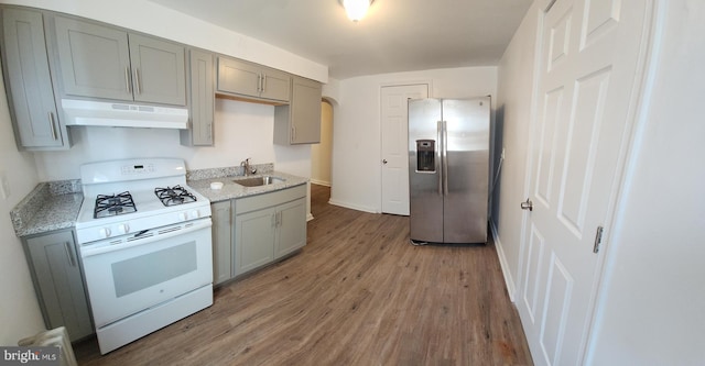 kitchen with sink, light stone counters, stainless steel fridge, white gas range, and hardwood / wood-style floors