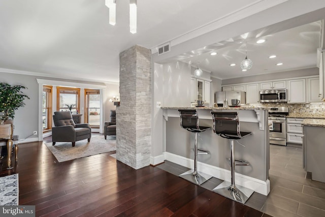 kitchen with a breakfast bar, ornate columns, white cabinetry, crown molding, and appliances with stainless steel finishes