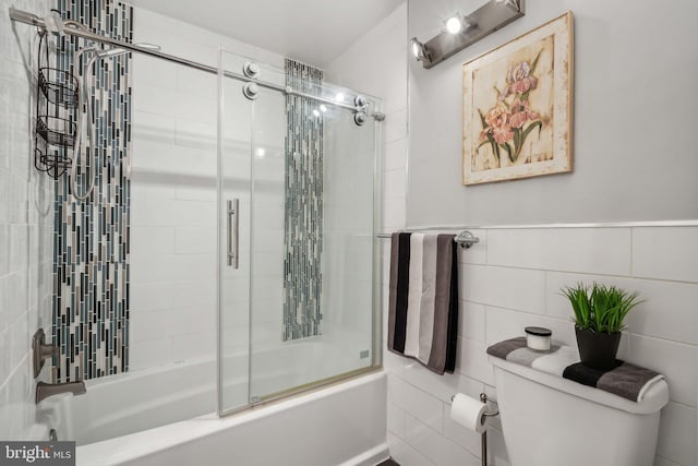 bathroom with tile walls, combined bath / shower with glass door, and toilet