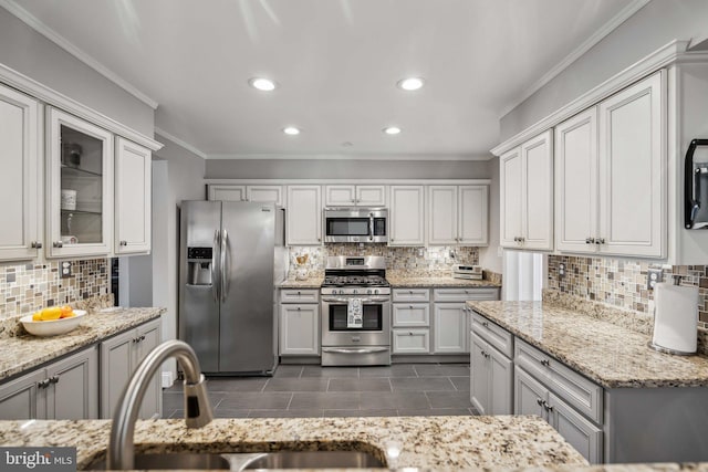 kitchen featuring sink, crown molding, appliances with stainless steel finishes, light stone counters, and decorative backsplash