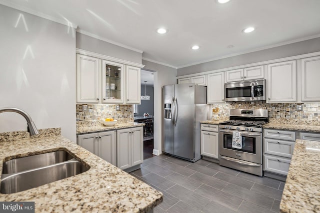 kitchen with sink, white cabinetry, stainless steel appliances, light stone counters, and ornamental molding