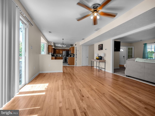 unfurnished living room with ceiling fan with notable chandelier and light hardwood / wood-style flooring