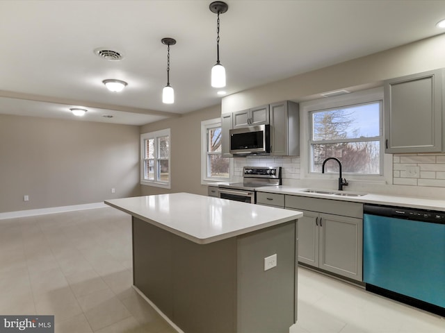 kitchen featuring stainless steel appliances, gray cabinets, sink, and a kitchen island