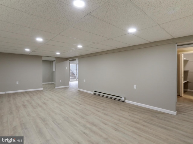 basement featuring light wood-type flooring, a paneled ceiling, and baseboard heating