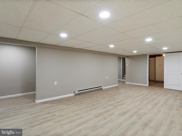 basement with a baseboard radiator, a paneled ceiling, and light hardwood / wood-style flooring