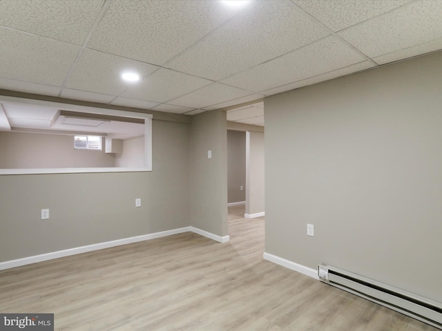 basement featuring a paneled ceiling, baseboard heating, and light hardwood / wood-style flooring