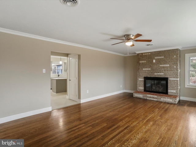 unfurnished living room with a brick fireplace, wood-type flooring, ornamental molding, and ceiling fan