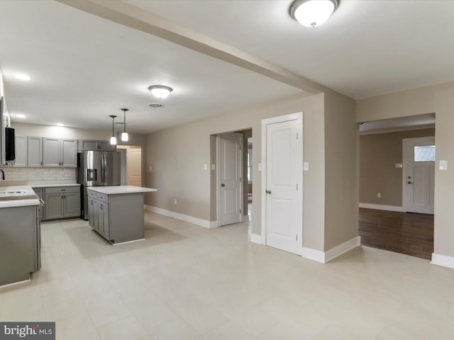 kitchen with pendant lighting, gray cabinets, backsplash, a kitchen island, and stainless steel fridge with ice dispenser