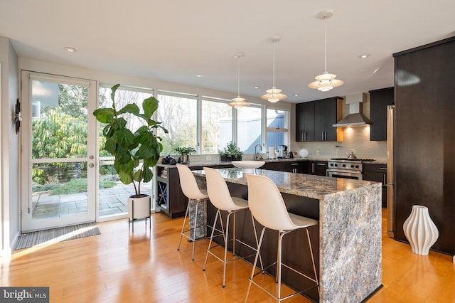 kitchen with a kitchen island, light stone countertops, pendant lighting, and wall chimney range hood