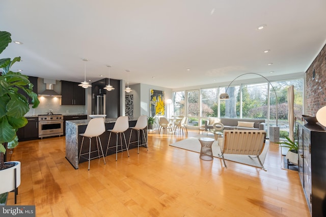 kitchen with light hardwood / wood-style floors, wall chimney exhaust hood, a center island, and stainless steel stove