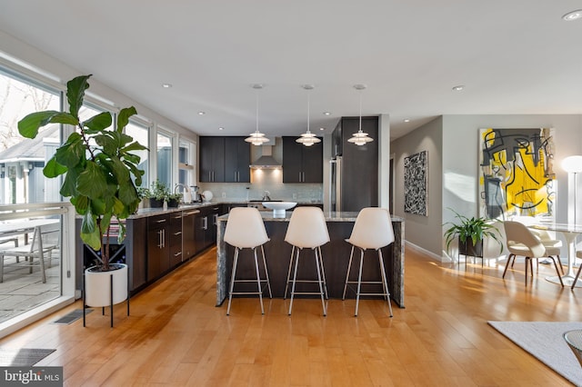 kitchen featuring a kitchen island, pendant lighting, light hardwood / wood-style flooring, a kitchen breakfast bar, and wall chimney exhaust hood