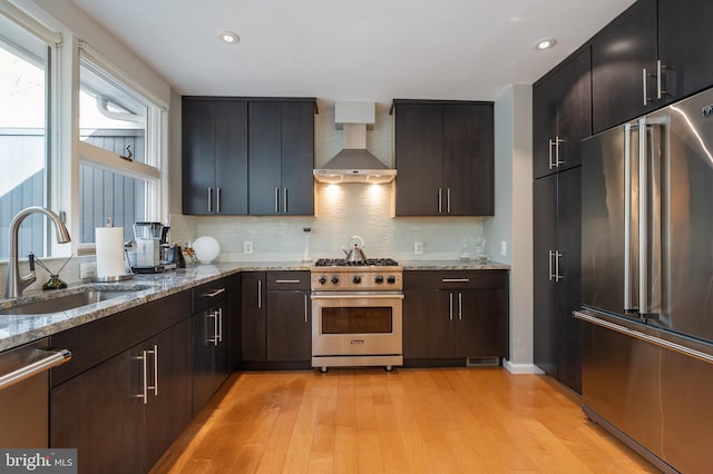 kitchen featuring high quality appliances, tasteful backsplash, sink, wall chimney range hood, and light wood-type flooring