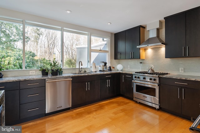 kitchen with sink, light hardwood / wood-style flooring, appliances with stainless steel finishes, light stone counters, and wall chimney exhaust hood