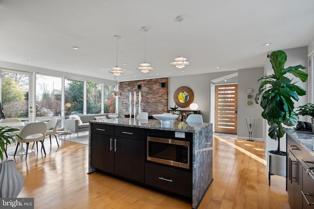 kitchen with stainless steel microwave, decorative light fixtures, light hardwood / wood-style floors, and stone countertops