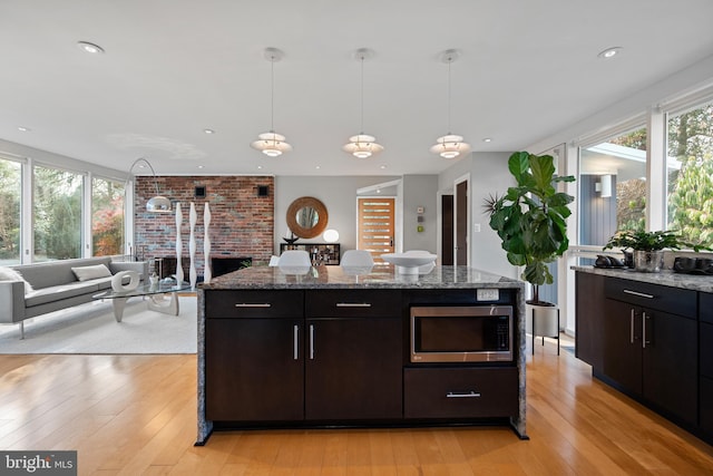 kitchen with dark brown cabinetry, light stone counters, light wood-type flooring, and decorative light fixtures