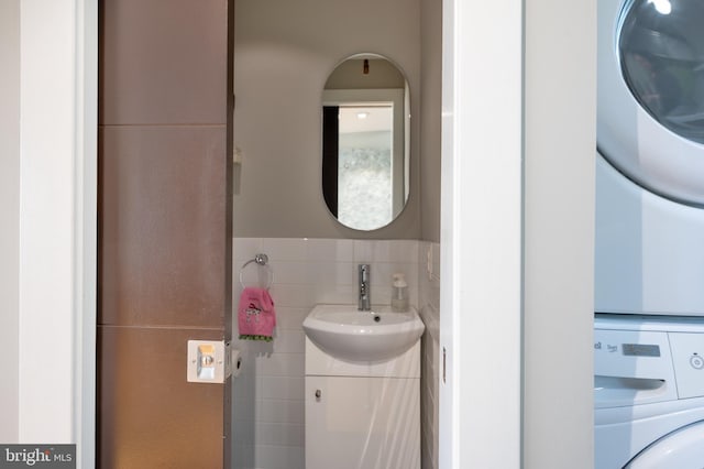 bathroom featuring vanity, stacked washer and clothes dryer, and tile walls