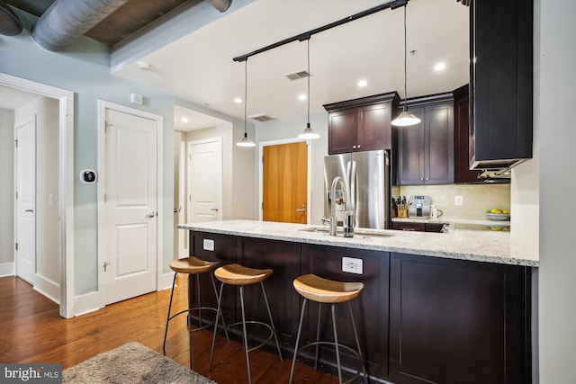 kitchen with stainless steel fridge, a breakfast bar area, backsplash, light stone countertops, and decorative light fixtures