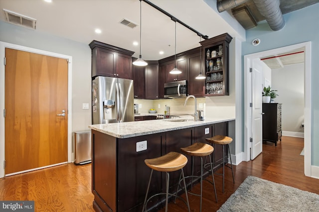 kitchen featuring sink, light stone counters, hanging light fixtures, appliances with stainless steel finishes, and a kitchen breakfast bar