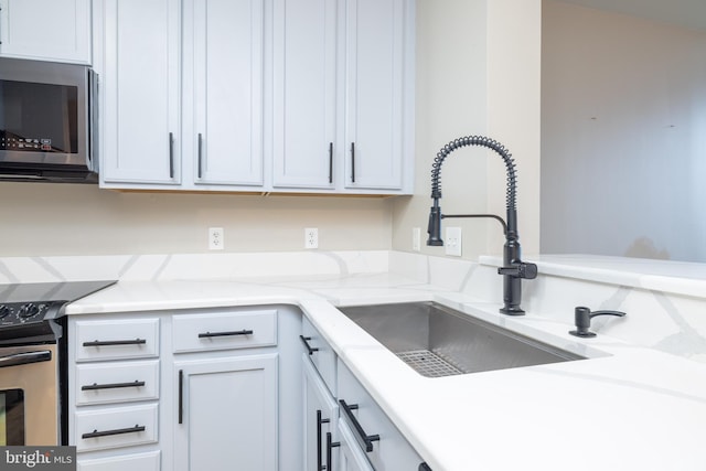 kitchen with appliances with stainless steel finishes, sink, white cabinets, and light stone counters