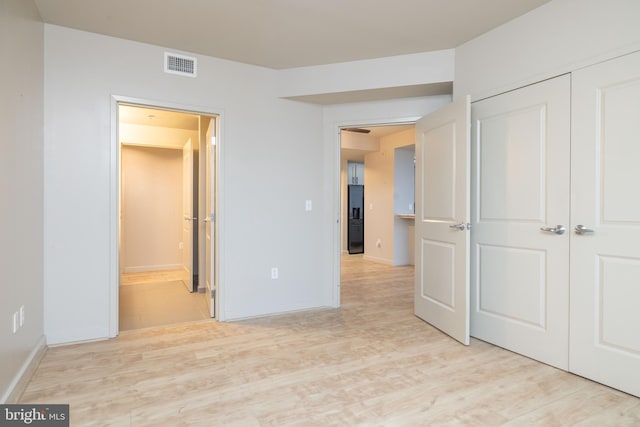 unfurnished bedroom featuring a closet, ensuite bath, and light hardwood / wood-style flooring